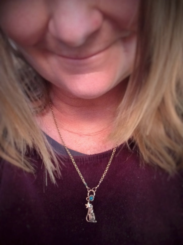 A close-up lifestyle shot of a person wearing a delicate gold chain necklace with a small pendant featuring a tiny blue stone and a star.