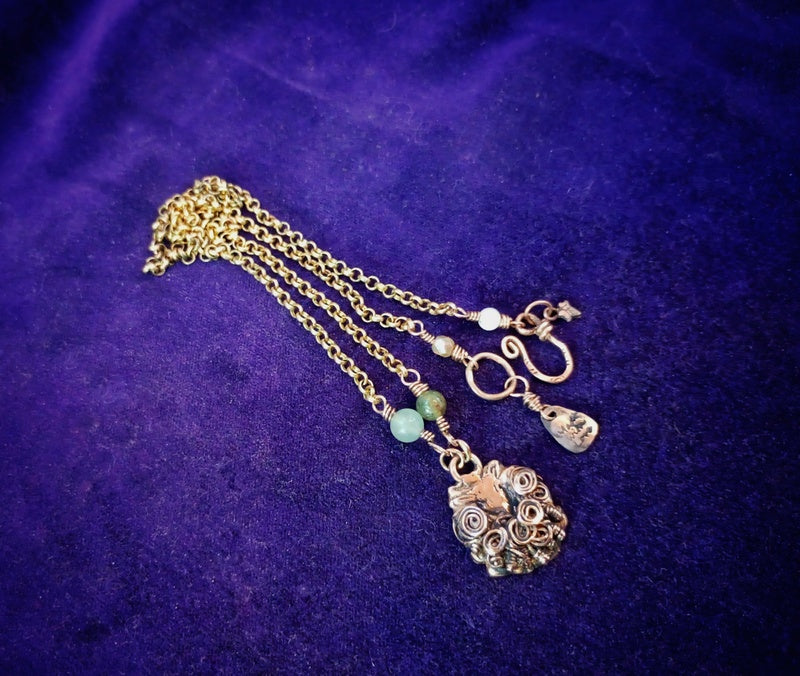 A gold-toned filigree necklace with a decorative pendant, shown on a textured purple velvet background.