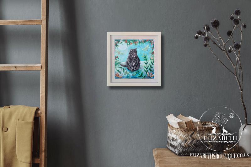 Framed artwork of a cat on a gray wall with a wooden shelf and decorative items.