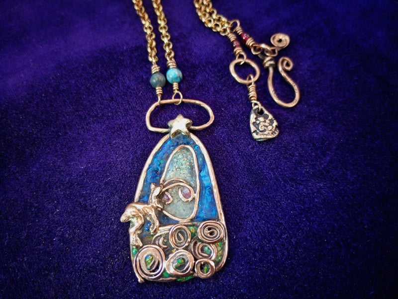 A handmade gold-toned pendant necklace featuring a star, a small horse figure, turquoise and green inlay, and coiled wire details, displayed on a dark purple velvet background.