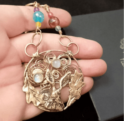 Bronze pendant with intricate design held in a hand against a dark background