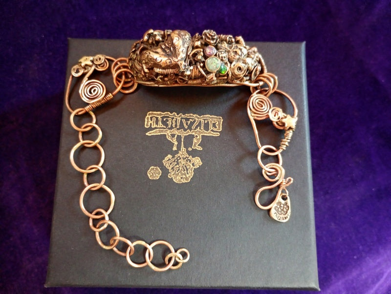 Bronze bracelet on a black box with 'Elizabeth' branding against a purple background