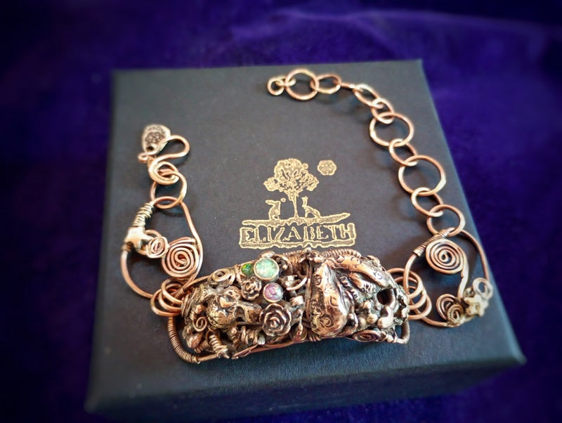 Elaborate copper bronze bracelet on a blue box with 'Elizabeth' branding against a purple background