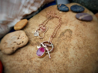 Bronze necklace with a pink ruby crystal pendant by Elizabeth Shewan jewellery designer from Dorset on a stone surface
