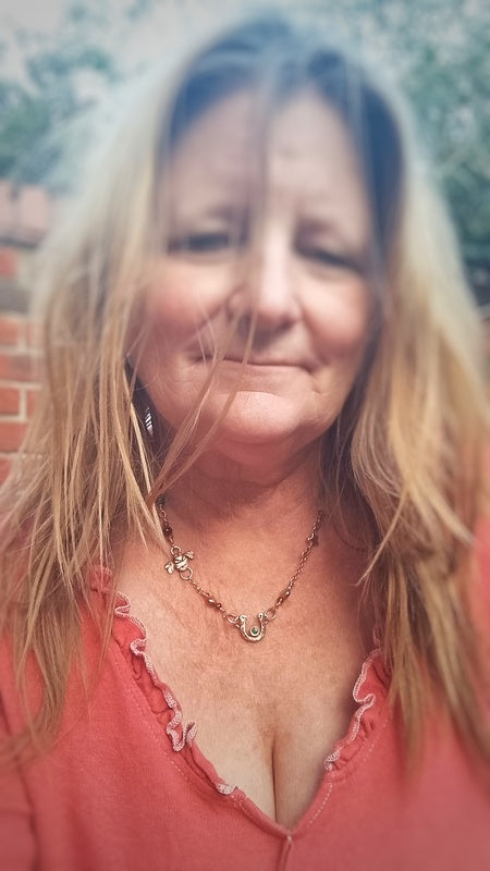 Woman with long blonde hair wearing a pink top and necklace, outdoors.