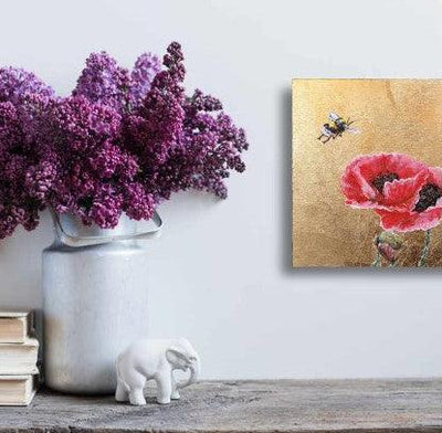 Decorative setting with a vase of purple flowers, a small white cat figurine, and a painting of a red poppy on a light gray surface.