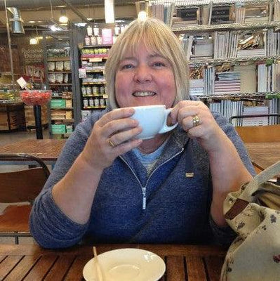 Person sitting at a table in a bookstore, holding a mug with text below about hares and a necklace.