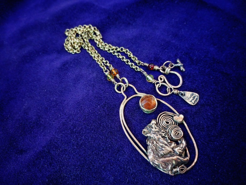 A silver-toned pendant necklace featuring a detailed animal motif and spiral wire accents, displayed on a deep blue velvet background.