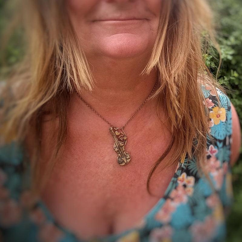 A close-up lifestyle shot of a woman wearing a bronze-toned pendant necklace with a stylized animal design, paired with a blue floral top.