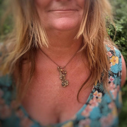 A close-up lifestyle shot of a woman wearing a bronze-toned pendant necklace with a stylized animal design, paired with a blue floral top.