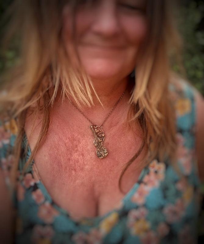 A close-up lifestyle shot of a woman wearing a delicate gold pendant necklace handmade by Elizabeth Shewan Jewellery Designer with a floral rose design, paired with a blue and pink floral top.