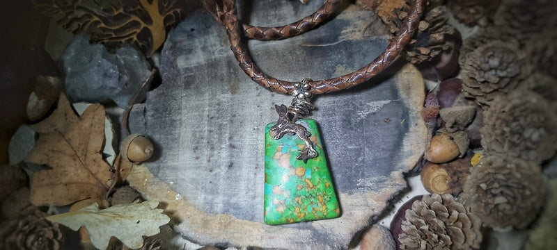 Necklace with a green pendant and brown leather cord on a stone background