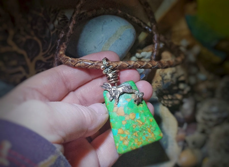 Necklace with a green stone pendant held by a hand against a natural background.