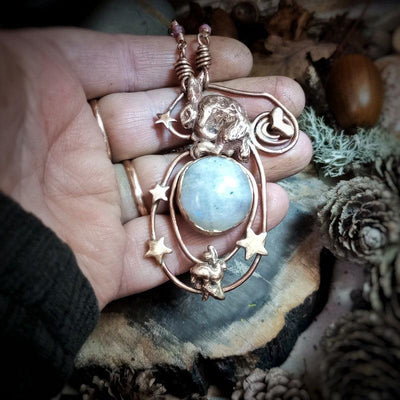 Hand holding a decorative pendant with a blue stone and gold accents on a natural background.