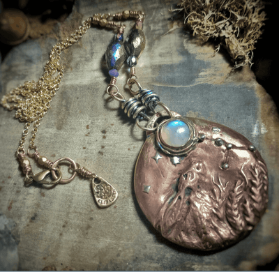 Handmade necklace with a bronze pendant and beaded chain on a textured surface