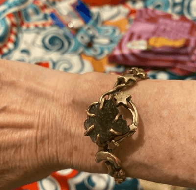 Bronze maldavite bracelet commission by artist Elizabeth Shewan metalsmith on a wrist with a colorful patterned background