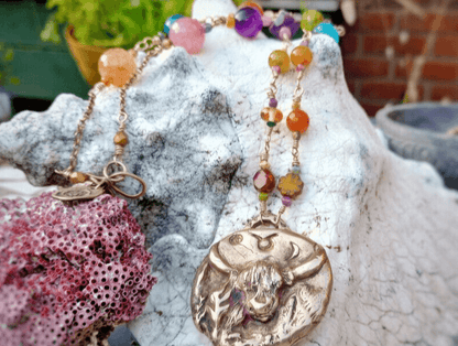 Zodiac Taurus bronze Pendant with a beaded crystal necklaces by Artist and Jewellery Designer Elizabeth Shewan on a textured stone surface, outside her studio in Dorset.