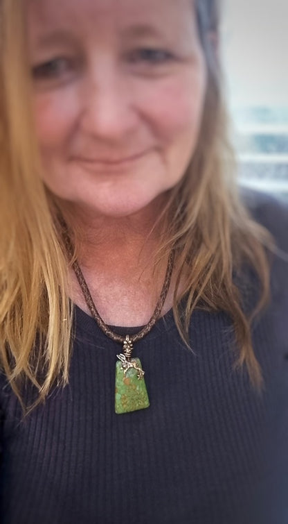 Person wearing a necklace with a green pendant against a blurred background