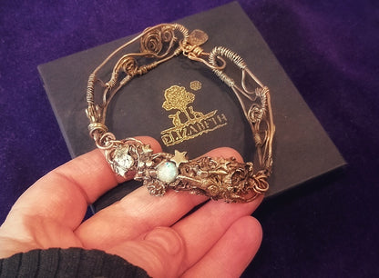 Gold bracelet with gemstones held by a hand on a dark background