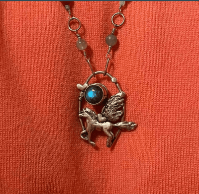 Necklace with a horse with wings pegasus and labradorite moon pendant on an orange fabric background