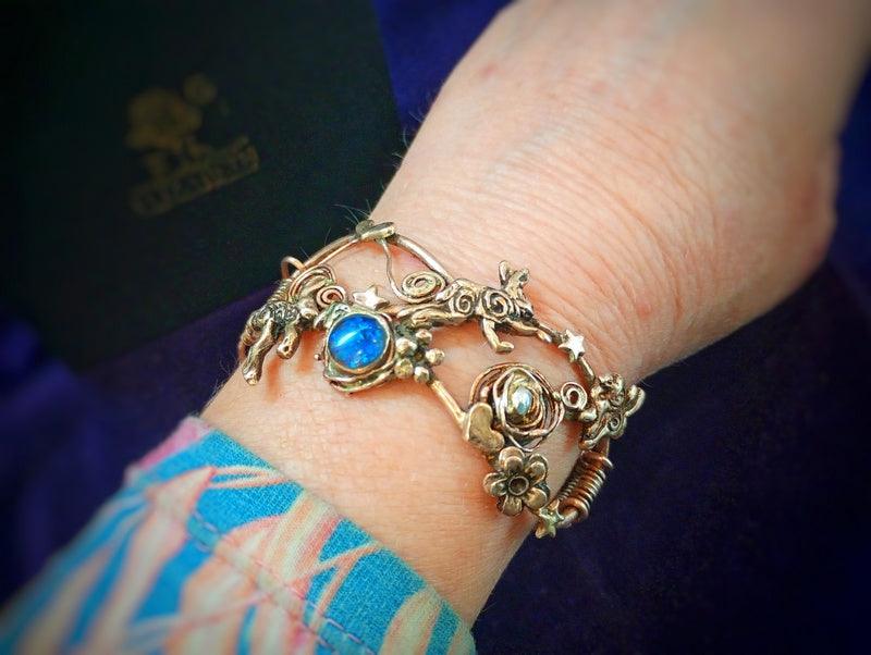 Decorative handmade bronze bracelet with blue opal gemstone on a wrist against a dark background by designer Elizabeth Shewan Boutique