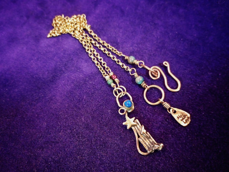 A gold-toned triple-strand chain necklace with a star and manger baby pendant, turquoise beads, and a hook clasp, displayed on a textured purple background.