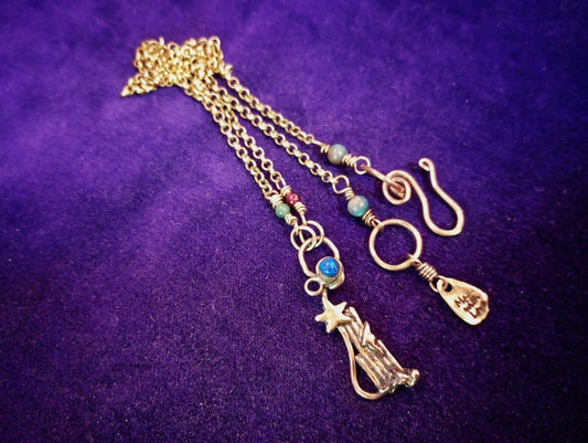 A gold-toned triple-strand chain necklace with a star and manger baby pendant, turquoise beads, and a hook clasp, displayed on a textured purple background.