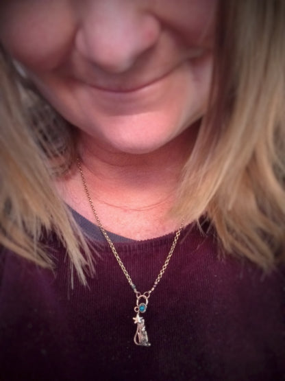 A close-up lifestyle shot of a person wearing a delicate gold chain necklace with a small pendant featuring a tiny blue stone and a star.