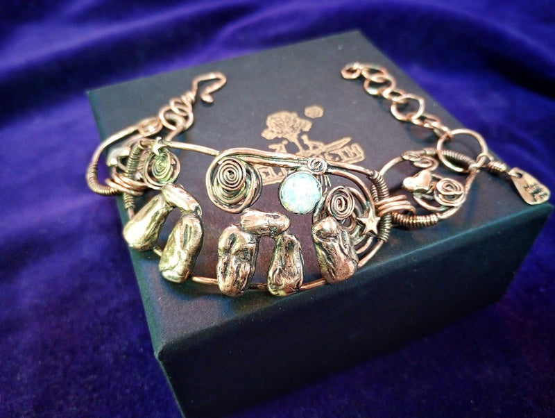 A handmade wire-wrapped bracelet with natural stone accents and a central round light blue stone, displayed on a dark velvet jewelry box. Stonehenge Bracelet.