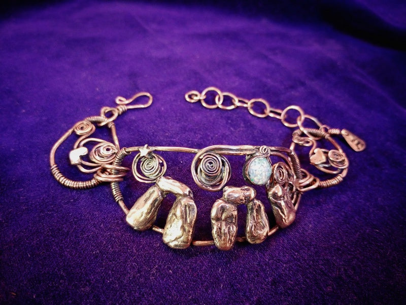 A handmade bohemian-style wire bracelet with natural-looking polished stones and spiral wire details, displayed on a textured purple fabric background.