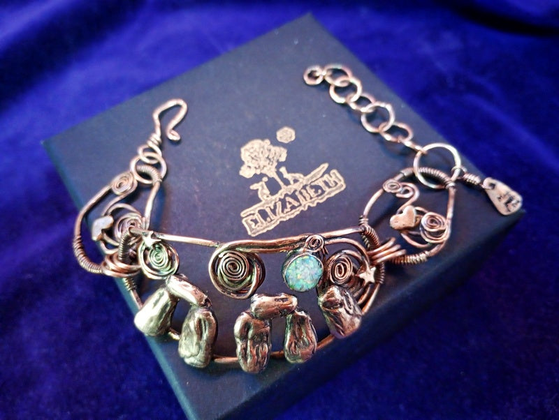 Stonehenge Bracelet. A handmade wire-wrapped bracelet with natural green stones and a turquoise-blue bead, displayed on a dark blue velvet box with a gold logo.