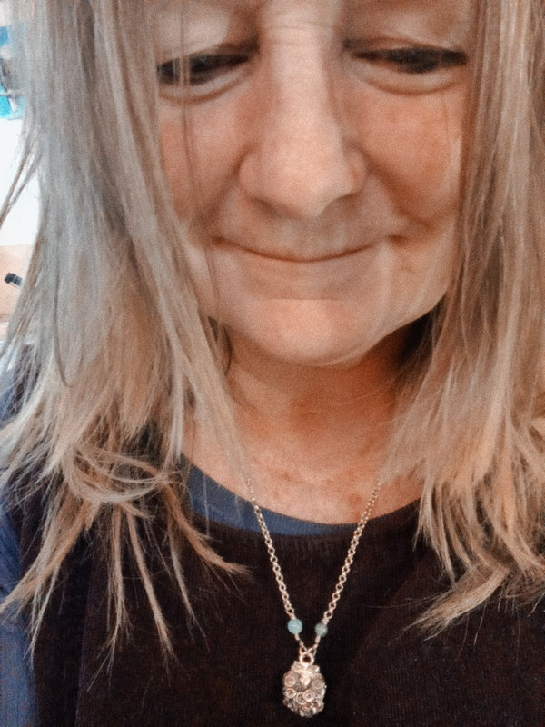 A close-up lifestyle shot of a woman wearing a delicate gold chain necklace with a clear faceted pendant and a small light blue bead accent.