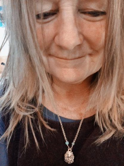 A close-up lifestyle shot of a woman wearing a delicate gold chain necklace with a clear faceted pendant and a small light blue bead accent.