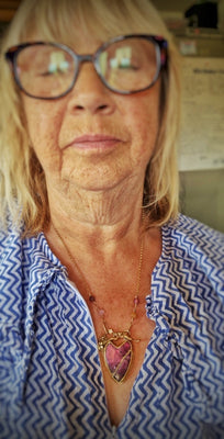 Woman wearing glasses and a blue patterned shirt with a heart-shaped pendant created as a commission by artist and jewellery designer Elizabeth Shewan, from her studio based in Dorset in England.
